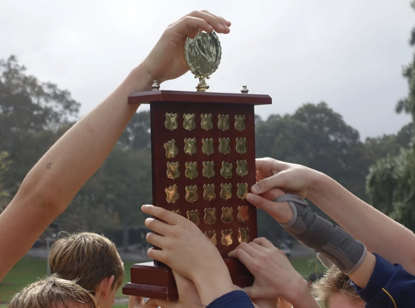 Team gathered around a large perpetual trophy outdoors.